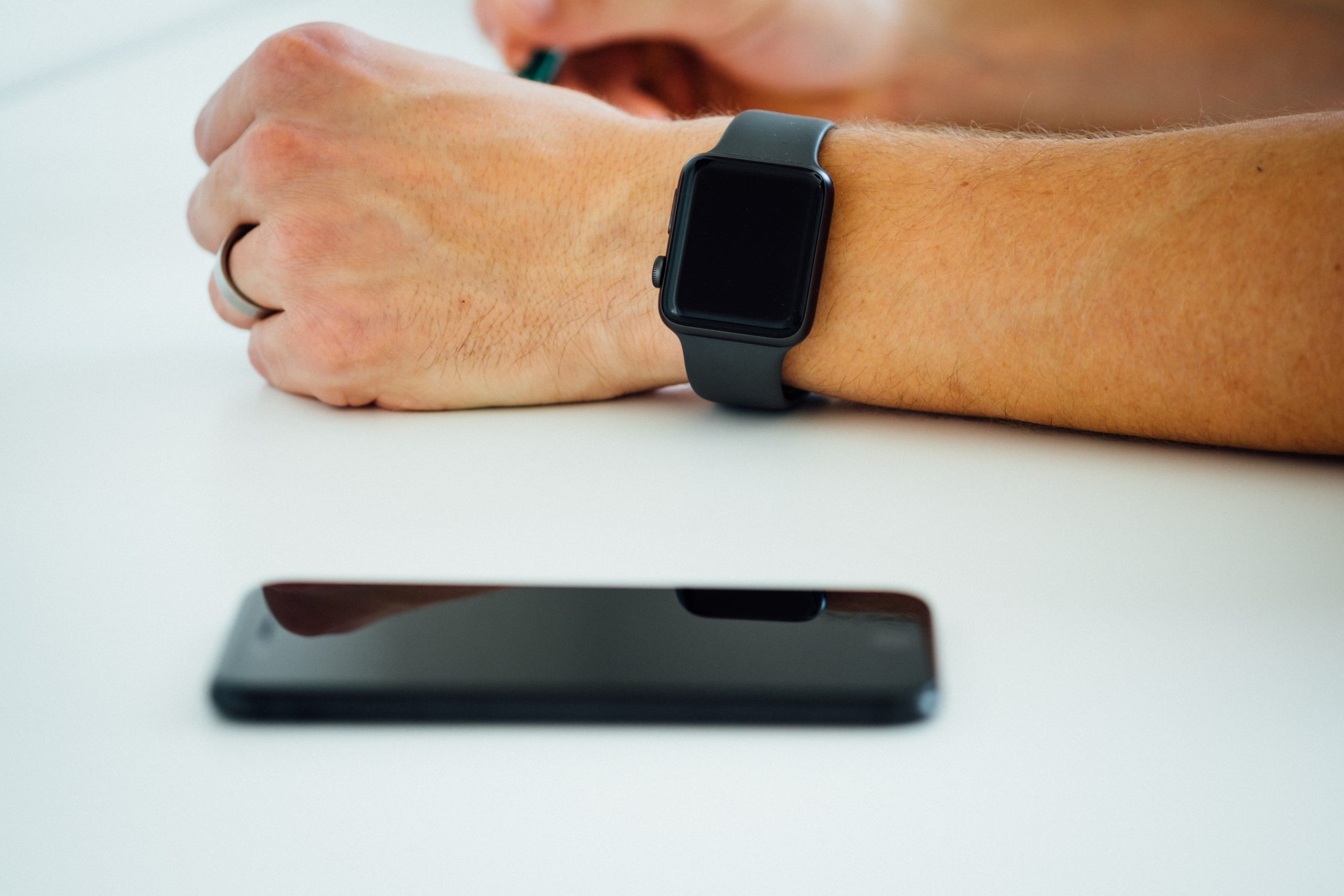 Detail of an arm of a man wearing a smartwatch next to his smartphone