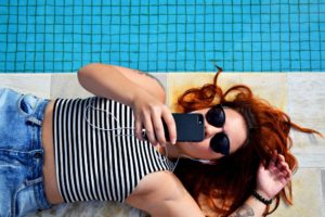 Young girl uses her smartphone lying by the pool